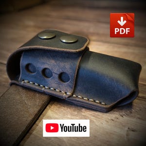 May include: A dark brown leather belt holster featuring a flap secured by two metallic snap buttons. The holster has a side panel with three circular cutouts and is constructed with visible light-colored stitching along the bottom edge.