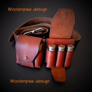 Peut inclure: Une ceinture en cuir marron avec une pochette à rabat et un support contenant trois cartouches de fusil. Le texte Woolenpaw design est visible dans les coins supérieur gauche et inférieur gauche de l'image.