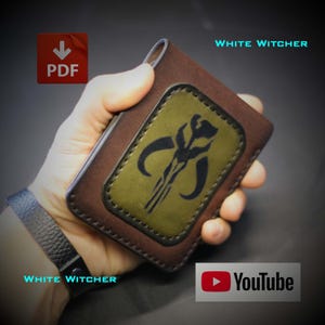 May include: A brown leather wallet featuring a rectangular olive green inlay with a black Mythosaur skull emblem. The wallet has dark brown stitching along the edges and is held in a hand. Text on the image includes PDF, White Witcher, and YouTube.
