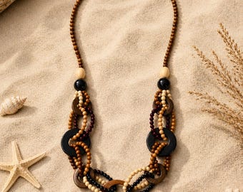 Op de afbeelding: Een meerstrengs ketting met een combinatie van kleine ronde houten kralen in tinten beige, donkerbruin en zwart, afgewisseld met grotere platte ronde houten ringen in bijpassende kleuren, gerangschikt in een gelaagd, trapsgewijs ontwerp.