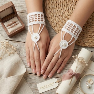 May include: A pair of white crochet fingerless gloves featuring a grid pattern on the wrist, a circular motif on the back of the hand, and a single central pearl accent. The gloves are designed to loop around the middle finger with delicate thread.