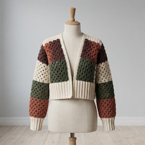 May include: A cropped cardigan featuring a granny square crochet pattern in blocks of cream, dark brown, olive green, and terracotta. The garment has long sleeves with ribbed cream cuffs and a matching ribbed cream hem along the open front edge.