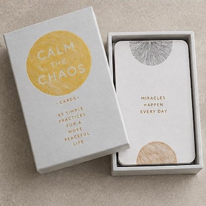 May include: A deck of cards in a light grey box with a yellow circle and the text CALM THE CHAOS 65 SIMPLE PRACTICES FOR A MORE PEACEFUL LIFE. The top card in the open box features a black sunburst graphic and the text MIRACLES HAPPEN EVERY DAY.