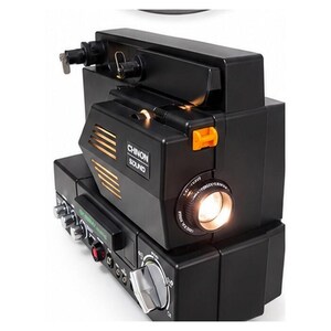 May include: A black Chinon Sound movie projector featuring a prominent lens, a rectangular body with ventilation slats, a bright internal light, and various silver control knobs and switches located on the side of the device.