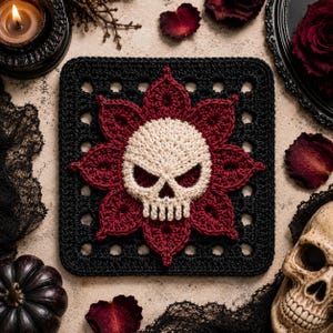 Könnte beinhalten: Ein quadratisches Häkelmotiv mit einem zentralen cremeweißen Totenkopf, umgeben von einem dunkelroten Blumenmuster, alles vor einem schwarzen quadratischen Hintergrund mit einem gitterartigen Rand. Das Design ist mit feinen Garnstichen gefertigt.