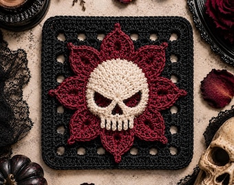 May include: A square crochet motif featuring a central off-white skull surrounded by a dark red floral pattern, all set against a black square background with a grid-like openwork border. The design is crafted with intricate yarn stitching.