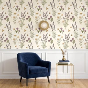 May include: A deep blue velvet armchair sits beside a gold metal side table with a small vase and books. The wall features cream-coloured wallpaper with a repeating pattern of purple lavender, white daisies, clover, and small honeybees.