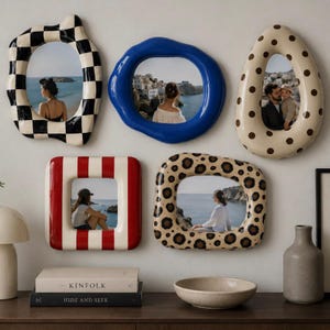 Puede incluir: Una colección de cinco espejos de pared con marcos irregulares y redondeados que presentan distintos patrones: tablero de ajedrez blanco y negro, azul sólido, beige con lunares marrones, rayas verticales rojas y blancas, y un estampado de leopardo.