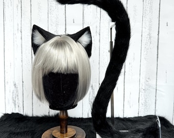 May include: A set of black faux fur cat ears with white inner accents, paired with a long, matching black faux fur tail. The ears are positioned on a mannequin head featuring a short, straight, platinum blonde bob wig with bangs.