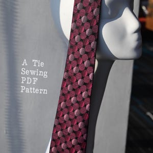 Puede incluir: Una corbata con un patrón repetitivo de círculos de color magenta oscuro y negro con un efecto de textura a rayas. El texto A Tie Sewing PDF Pattern es visible en el lado izquierdo de la imagen, junto a la corbata sobre una cabeza de maniquí blanca.
