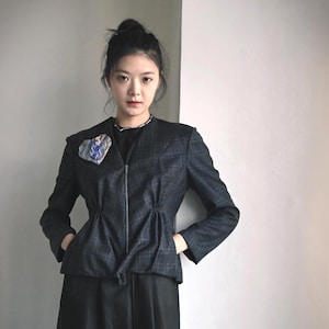 May include: A dark charcoal grey plaid blazer featuring a front zip closure, long sleeves, and gathered waist detailing. A decorative heart-shaped patch with a blue and white patterned fabric is attached to the upper right chest area.