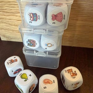 Op de afbeelding: Een set witte SpeechStackers-kunststofdobbelstenen met kleurrijke illustraties van objecten en bijbehorende tekstlabels zoals drum, dress, chair, pear, ear en tiger. De dobbelstenen zitten in doorzichtige, stapelbare kunststof bakjes met R-blends tekst.