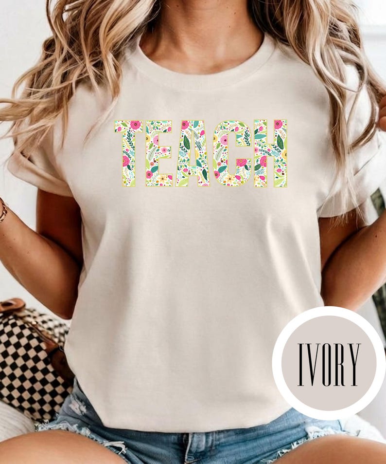 Pu&ograve; includere: Una t-shirt a maniche corte color avorio con la parola TEACH stampata in grandi lettere maiuscole. Le lettere sono riempite con un colorato motivo floreale composto da fiori rosa, gialli e blu mescolati a foglie verdi su sfondo bianco.