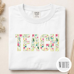 Pu&ograve; includere: Una t-shirt bianca con la parola TEACH stampata in grandi lettere maiuscole. Le lettere sono riempite con un colorato motivo floreale composto da fiori rosa, gialli e rossi con foglie verdi. Un'etichetta Comfort Colors &egrave; sul colletto.