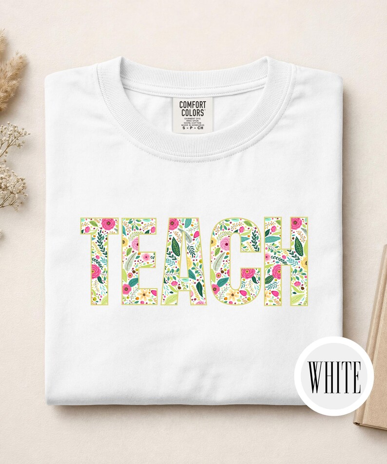 Pu&ograve; includere: Una t-shirt bianca con la parola TEACH stampata in grandi lettere maiuscole. Le lettere sono riempite con un colorato motivo floreale composto da fiori rosa, gialli e rossi con foglie verdi. Un'etichetta Comfort Colors &egrave; sul colletto.