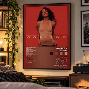 May include: A framed music poster featuring Aaliyah on a red background. The poster displays the artist name, album title, tracklist, release date of 7th July 2001, a 62-minute length, and a colour palette of black, red, mauve, and light pink.
