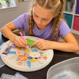 May include: A round diamond painting kit featuring a colorful floral design with various shades of pink, orange, blue, and yellow. The kit includes a pink applicator tool, a green tray, a tube of B-7000 adhesive, and multiple bags of small beads.