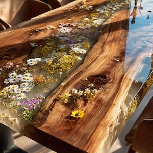 May include: A rectangular dining table featuring a live edge wood slab with a central river of clear resin embedded with various dried wildflowers, including white daisies and yellow blossoms, supported by dark metal legs.