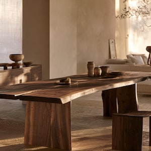 Puede incluir: Una mesa de comedor rectangular grande hecha de madera marrón oscura con un borde natural en los lados. La mesa cuenta con dos patas gruesas de losa vertical y se acompaña de taburetes de madera a juego con asientos curvos.