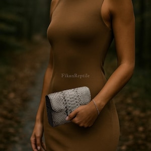 May include: A sleeveless brown dress paired with a rectangular clutch featuring a grey and white snakeskin texture. The clutch has a flap closure and the text FikanReptile is visible on the dress fabric above the bag.