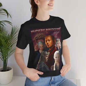 Puede incluir: Una camiseta negra de manga corta con un estampado gráfico que incluye el texto PHOEBE BRIDGERS en una fuente estilizada en la parte superior. El diseño muestra un collage de varias figuras de cabello claro y la silueta de un dragón sobre un fondo rojo.