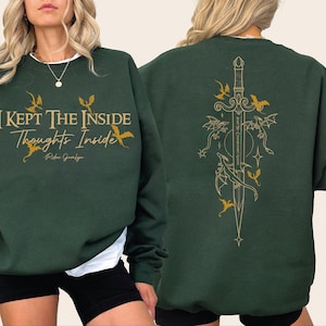 May include: A dark green crewneck sweatshirt featuring gold text on the front that reads I KEPT THE INSIDE Thoughts Inside and a script signature. The back displays a large gold graphic of a sword surrounded by several small flying dragons.