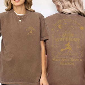 A woman wearing a brown t-shirt with text and graphics related to Salem Apothecary.