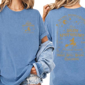two women wearing blue t-shirts with gold text and graphics on the back.