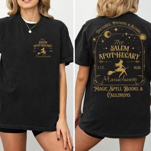 a woman wearing a black t-shirt with a graphic design on the back. The design includes text and a depiction of a witch on a broomstick.