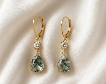 May include: A pair of gold leverback earrings featuring a small round clear gemstone above a teardrop-shaped moss agate stone with green inclusions. The earrings are crafted with a gold metal setting and secure leverback closures.