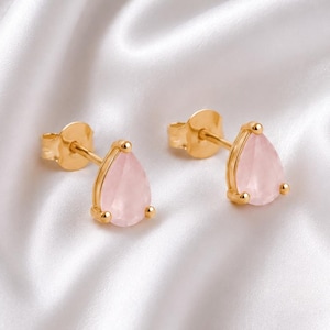 Puede incluir: Un par de pendientes de botón en oro con piedras preciosas de color rosa claro en forma de lágrima. Cada pendiente tiene un engaste de oro pulido que sujeta la piedra, con un poste y cierre de mariposa a juego visibles en el lateral.