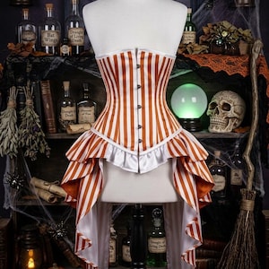 May include: A corset featuring vertical orange and white stripes with a front button closure. The garment includes a white ruffled trim along the waistline and a high-low hemline with cascading fabric panels that extend down the sides and back.