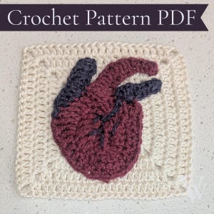 May include: A square crochet pattern PDF featuring a cream-colored granny square base with a dark red and charcoal gray anatomical heart motif stitched in the center. The text Crochet Pattern PDF is displayed in white on a dark purple banner.