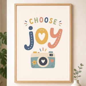 May include: A framed wall art print featuring the text CHOOSE JOY in colorful, rounded letters. The word JOY is stylized with a heart in the center of the O. Below the text is a light blue camera illustration with a heart lens, a star, and a heart.