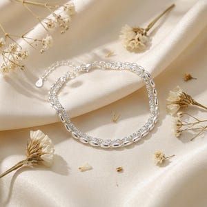 May include: A double-strand silver bracelet featuring one chain of smooth, polished oval beads and a second chain of small, sparkling clear stones. The bracelet includes a delicate extender chain with a small, flat, circular metal tag at the end.