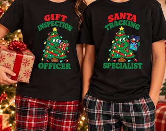 Peut inclure: Deux t-shirts noirs avec des graphismes de sapins de Noël. Le t-shirt de gauche porte l'inscription GIFT INSPECTION OFFICER avec un sapin tenant un cadeau. Celui de droite affiche SANTA TRACKING SPECIALIST avec un sapin tenant un téléphone.