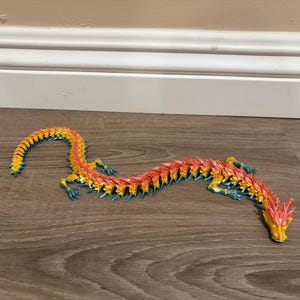 May include: A long, articulated dragon figurine featuring a vibrant gradient color scheme that transitions from yellow to orange, red, and blue. The creature has a segmented body, multiple small legs, and a detailed head with horn-like protrusions.