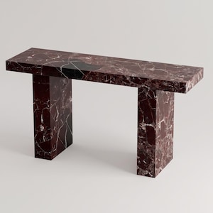 May include: A rectangular console table constructed from deep red marble with prominent white and dark grey veining. The piece features a flat, horizontal top surface supported by two thick, vertical rectangular legs, creating a clean, geometric form.