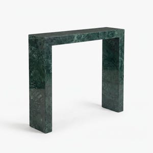 Peut inclure: Une console rectangulaire fabriquée en marbre vert foncé avec des veines naturelles visibles sur toute la surface. La pièce présente un design en forme de U continu avec un plateau plat et deux supports latéraux verticaux, arborant une finition polie.