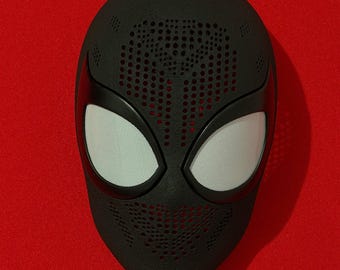 May include: A black full-face mask featuring a textured surface with a perforated pattern across the forehead and chin areas. The mask includes two large, almond-shaped eye openings covered with a fine, light-colored mesh material.