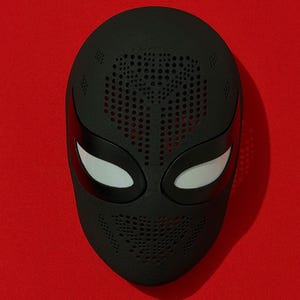 May include: A matte black full-face mask featuring a textured surface with numerous small circular perforations across the forehead and mouth areas. The mask includes two almond-shaped eye openings with white mesh lenses framed by smooth black borders.