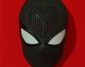 May include: A black full-face mask featuring a textured surface with numerous small circular perforations across the forehead and mouth areas. The mask includes two large, almond-shaped eye openings covered with a fine, light-colored mesh screen.