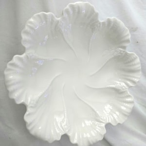 May include: A white ceramic bowl shaped like a flower with six distinct, ruffled petals. The surface features embossed, swirling lines that radiate from the center toward the edges, creating a textured, organic appearance with a glossy finish.