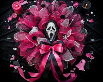 Pode incluir: Uma guirlanda decorativa com camadas de malha rosa choque, branca e preta, acentuada com pequenas rosas pretas e ornamentos de estrelas prateadas. Uma máscara Ghostface branca está centralizada, com um grande laço de fita de cetim rosa e preto.