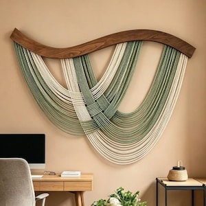 May include: A wall hanging featuring a curved dark wood top piece with multiple strands of cream and sage green cord draped in overlapping, layered loops that create a symmetrical, flowing pattern across the surface of the wall.