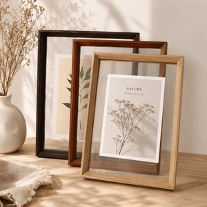 May include: Three rectangular floating picture frames in dark brown, medium brown, and light oak wood finishes. Each frame holds a vertical print featuring botanical illustrations. The front-most frame displays a print with the text NATURE botanical mood.