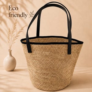 Pu&ograve; includere: Una borsa tote in paglia intrecciata con un'apertura ampia e un bordo nero lungo il margine superiore. La borsa presenta due manici neri e include la scritta Eco friendly stampata sul lato. Il corpo della borsa ha una finitura naturale beige.