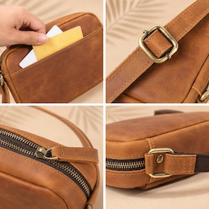 May include: A brown leather crossbody bag featuring a smooth matte finish, an exterior slip pocket, a top zipper closure with a matching leather pull tab, and an adjustable strap secured by antique brass-toned metal buckles and hardware.