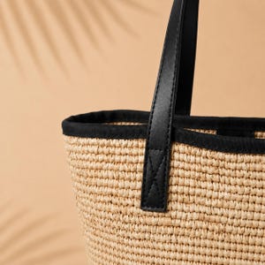 Pu&ograve; includere: Una borsa tote in paglia intrecciata con un corpo testurizzato color marrone chiaro naturale e un bordo in tessuto nero a contrasto lungo la parte superiore. La borsa presenta un robusto manico nero fissato con cuciture visibili e nette.