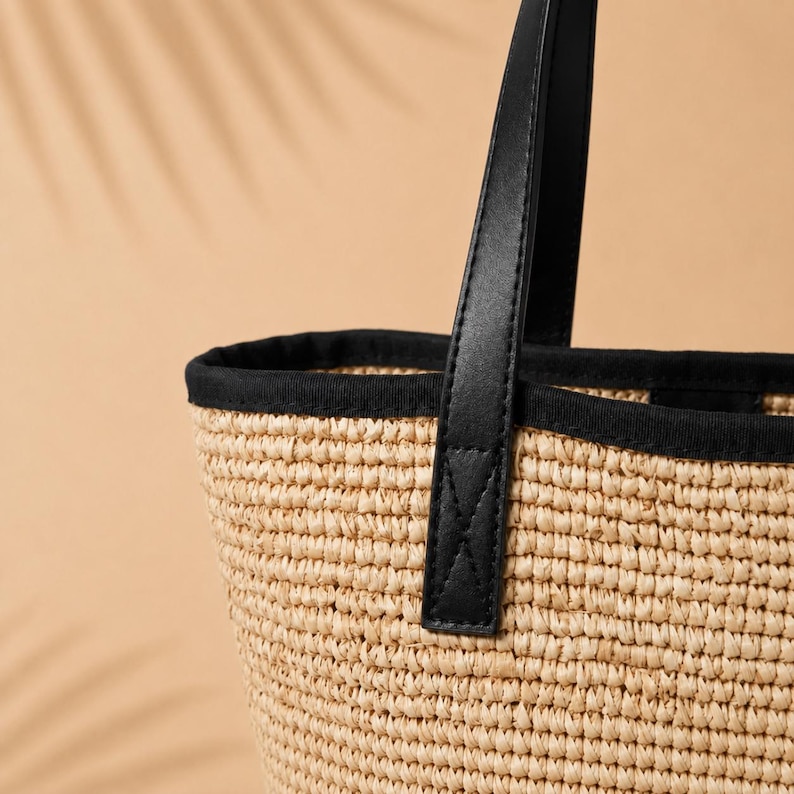 Pu&ograve; includere: Una borsa tote in paglia intrecciata con un corpo testurizzato color marrone chiaro naturale e un bordo in tessuto nero a contrasto lungo la parte superiore. La borsa presenta un robusto manico nero fissato con cuciture visibili e nette.